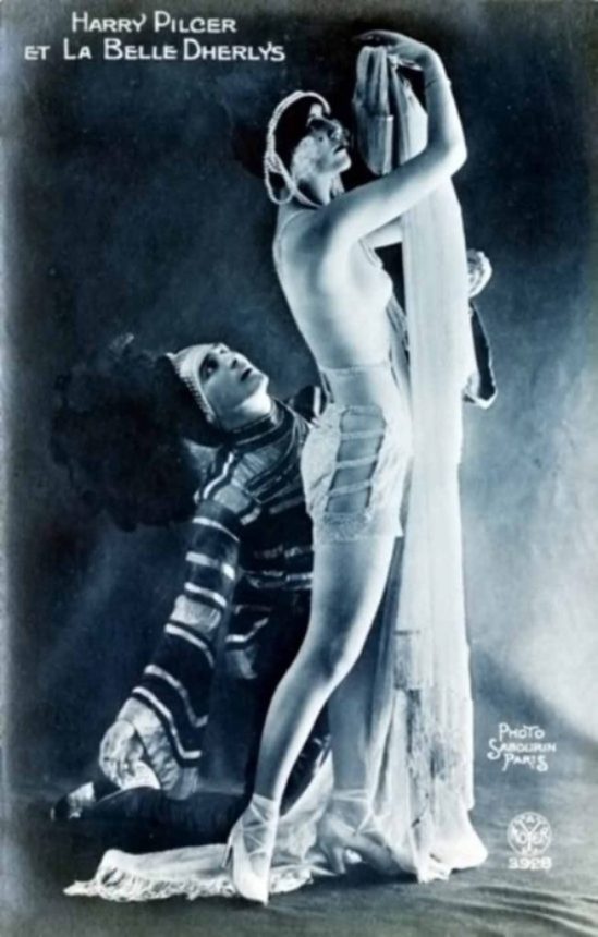 Alfred Noyer. The topless performer La Belle Dherlys, wearing a long string of pearls around her head, and the American dancer Harry Pilcer during a performance at the Revue du Casino de Paris.1st March 1921. Via getty