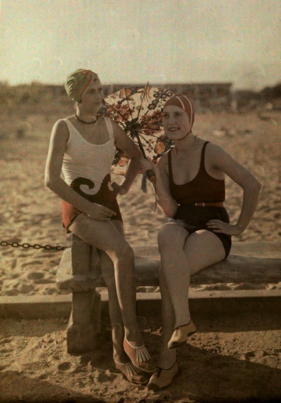 Two women in bathing suits sit on a bench.